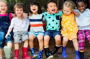 Children smiling and laughing sitting on a brick wall outside in colorful clothing.