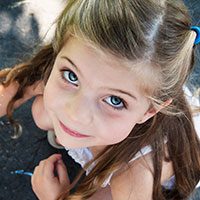 Young child smiling outside playing with chalk.